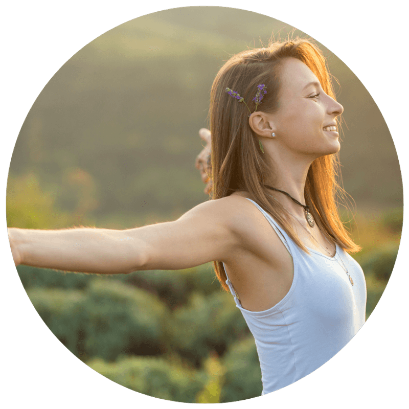 A woman standing outdoors with her arms open wide, smiling — a sense of freedom and clarity