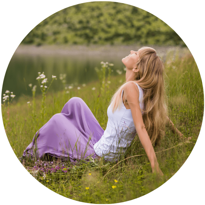 A woman sitting peacefully in a sunlit meadow, looking upward with calm